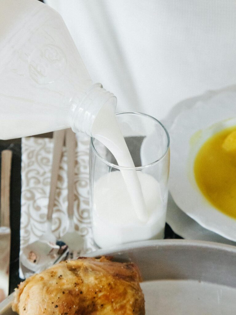 Close-up of milk being poured into a glass next to a chicken dish.